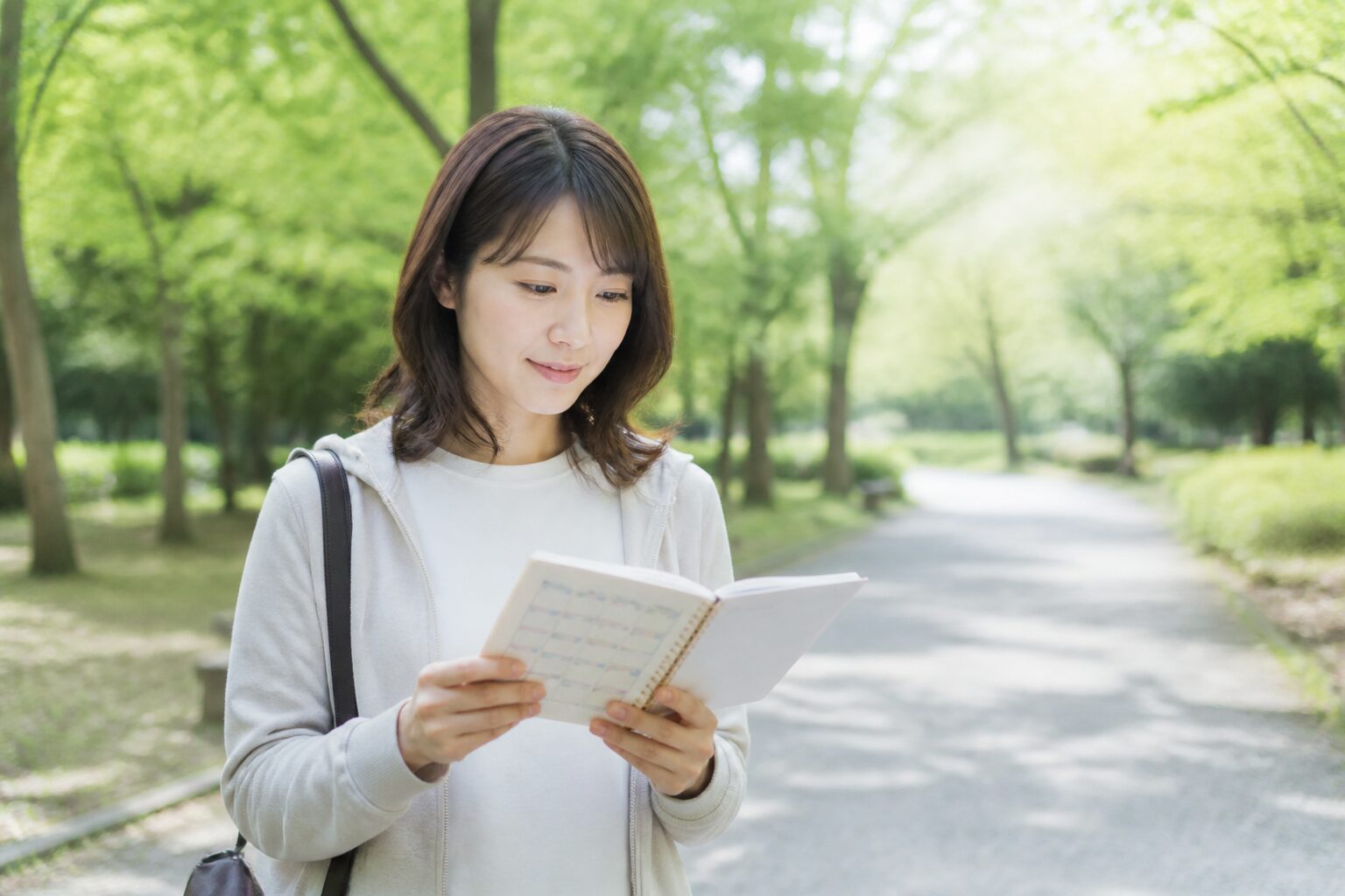 公園の朝の光の中で新しい予定を確認する30代女性
