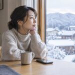 冬の窓辺で外を眺める女性