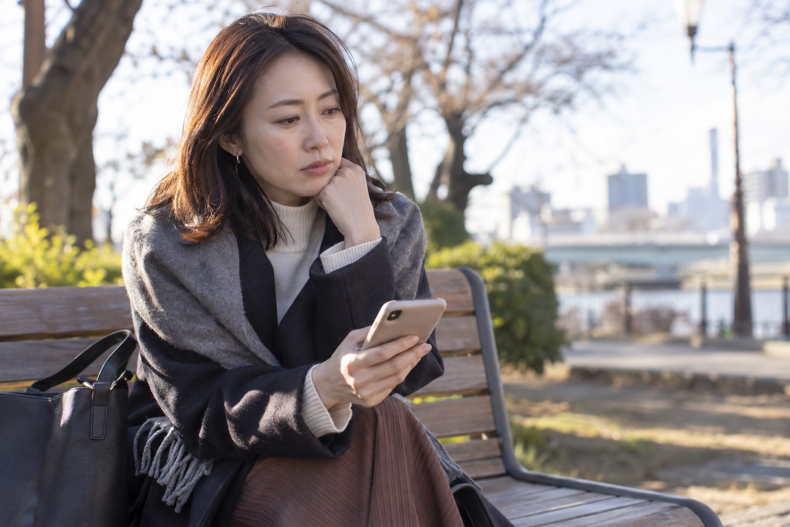 公園でスマートフォンを見ながら考える女性
