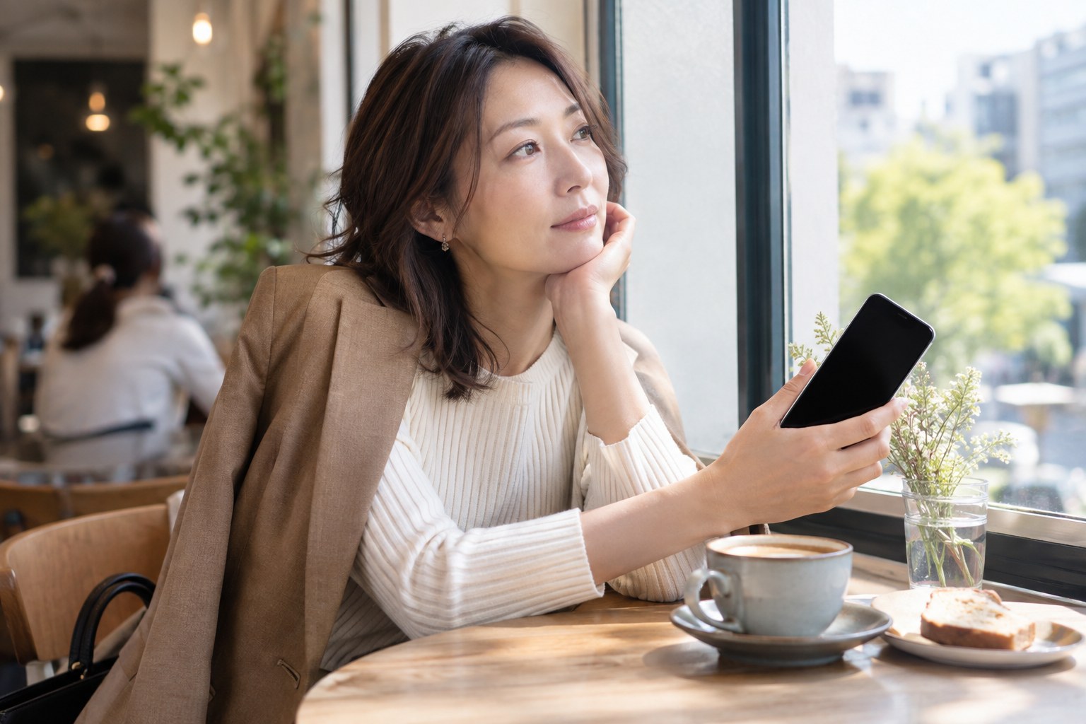 窓辺でスマートフォンを手に考える女性